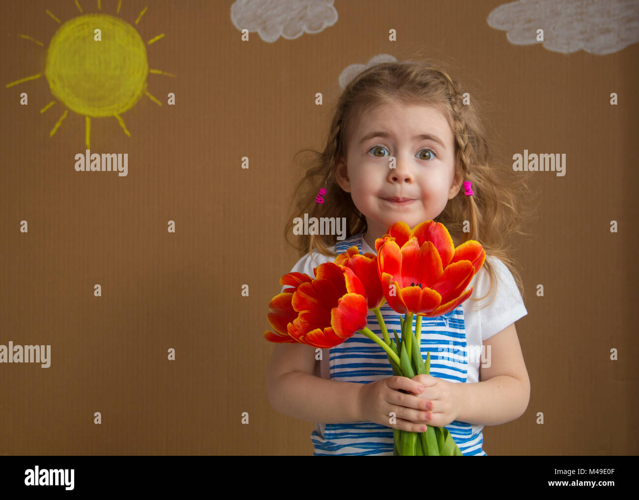 Portrait psychologique belle fille de la robe bleue avec des fleurs tulipes en mains sur un fond clair avec soleil et nuages peints Banque D'Images