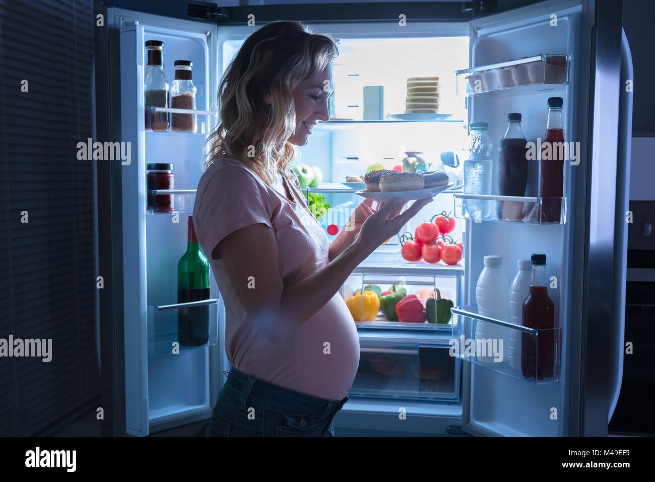 Young Happy pregnant woman Holding Plate Of Cookies dans la cuisine près de réfrigérateur Banque D'Images