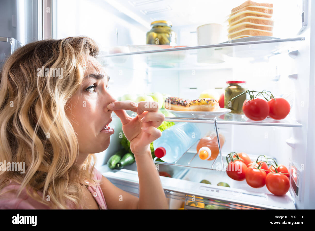Close-up of a Young Woman Holding Her Nose près de mauvais aliments dans réfrigérateur Banque D'Images