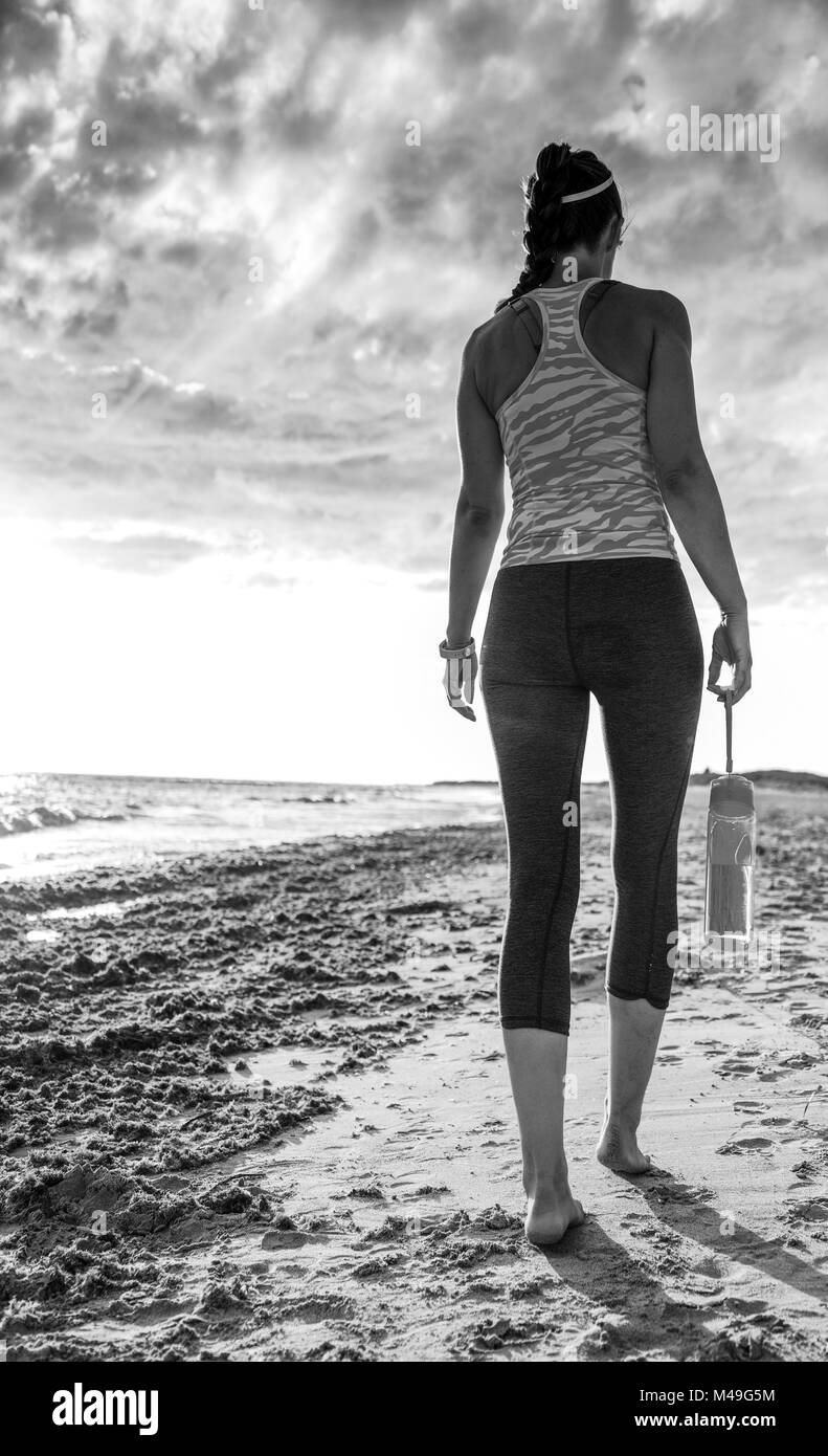 Côté mer sauvage rafraîchissante d'entraînement. Vus de derrière, jeune femme en bonne santé dans les vêtements de sport sur la plage à pied Banque D'Images