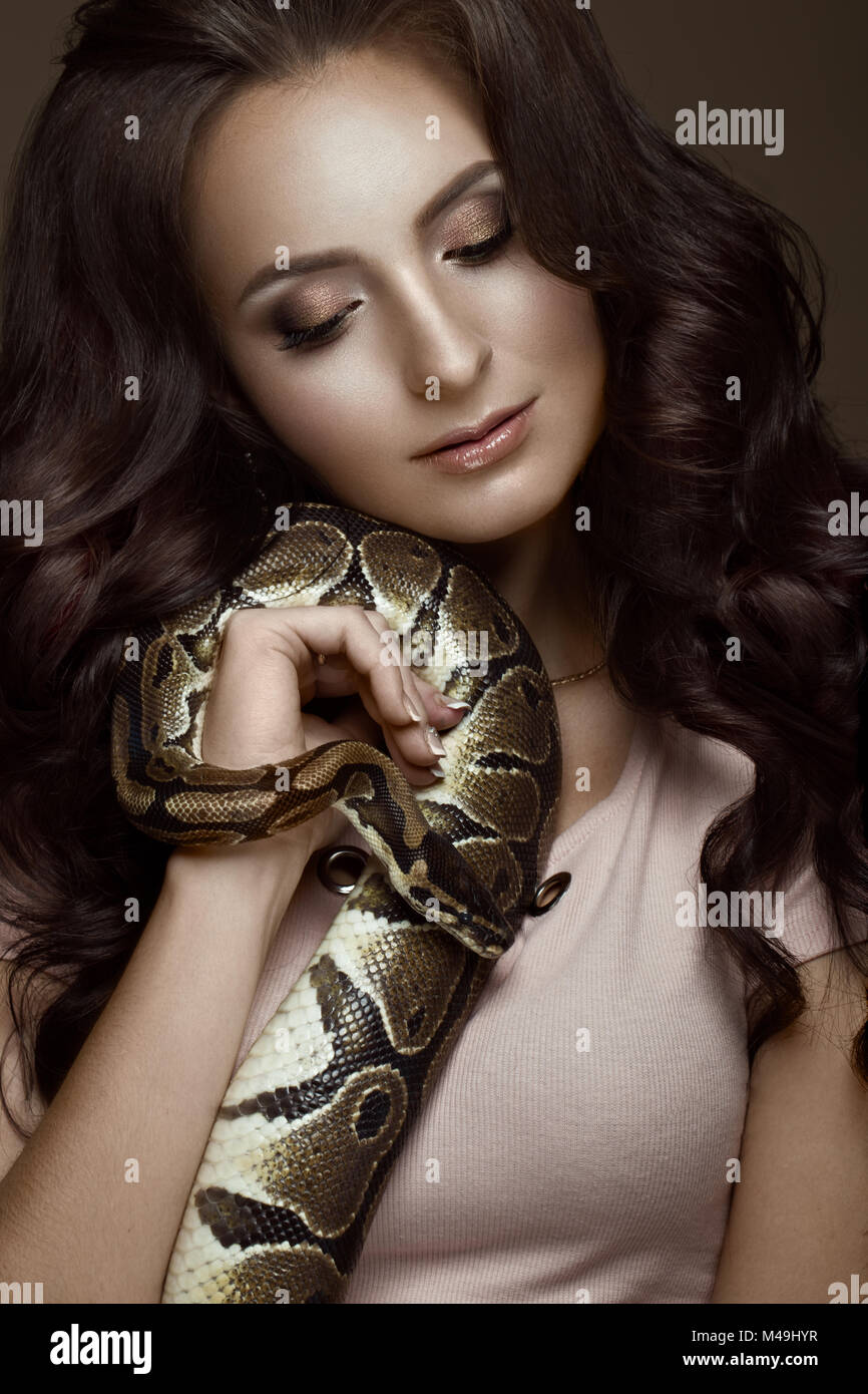 Belle fille brunette model, boucles parfaite et soirée fashion make-up avec un serpent dans ses mains. Beauté Visage. Banque D'Images