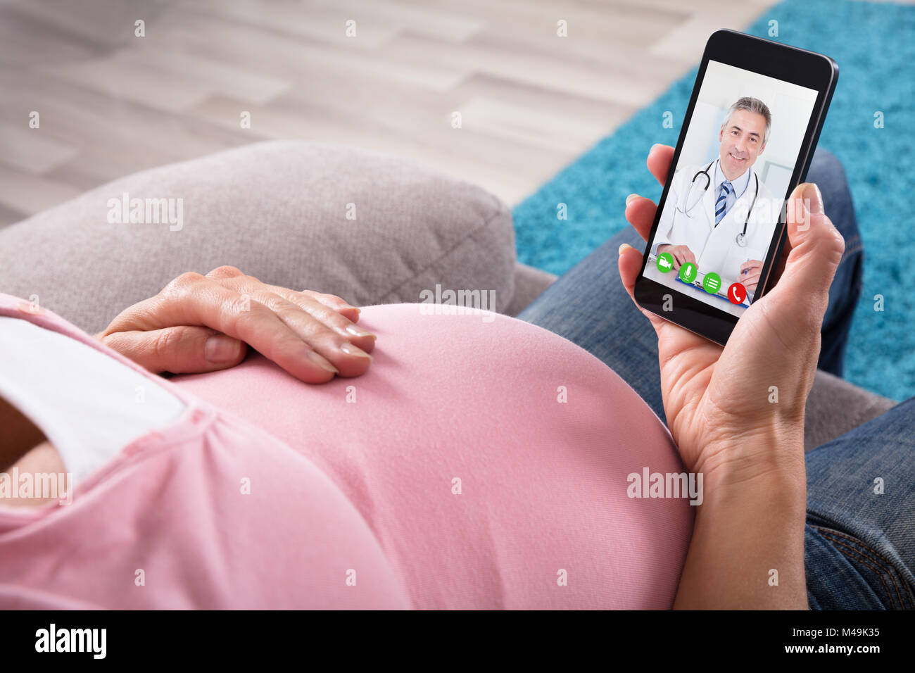 Close-up of pregnant woman Sitting attendent Sur Canapé la visioconférence avec médecin sur téléphone mobile Banque D'Images