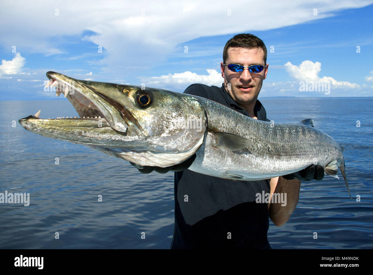 Heureux fisherman holding un magnifique baraccuda. La pêche en haute mer, pêche au gros, des prises de poissons. Banque D'Images