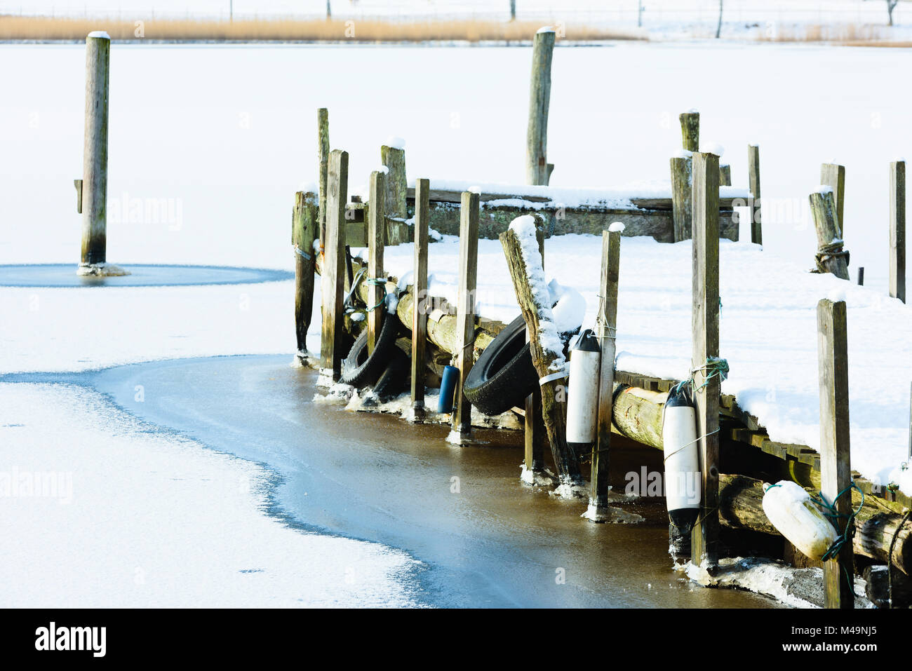 Ancienne jetée en bois dans la glace et la neige. Les poteaux d'amarrage le long de la côte et en mer. Rive opposée visible à travers la baie. Banque D'Images