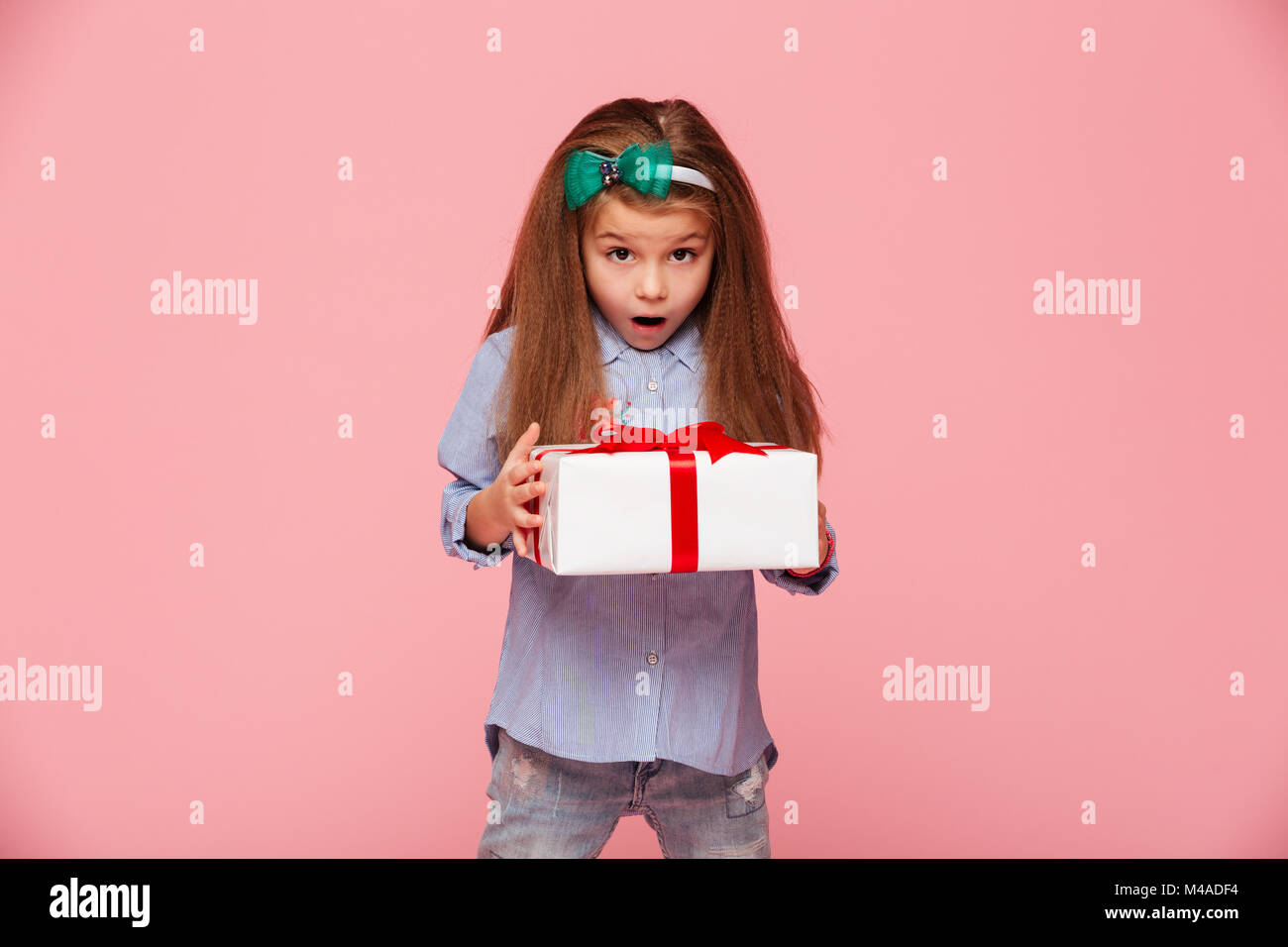 Jolie fille 5-6 ans holding present fort avec la bouche ouverte, d'être heureux et surpris de recevoir le cadeau d'anniversaire sur fond rose Banque D'Images