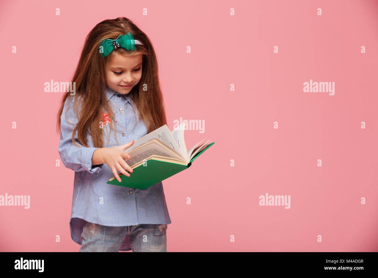 Image de smart lycéenne 5-6 ans avec longs cheveux auburn, lecture livre intéressant plus isolé sur fond rose Banque D'Images