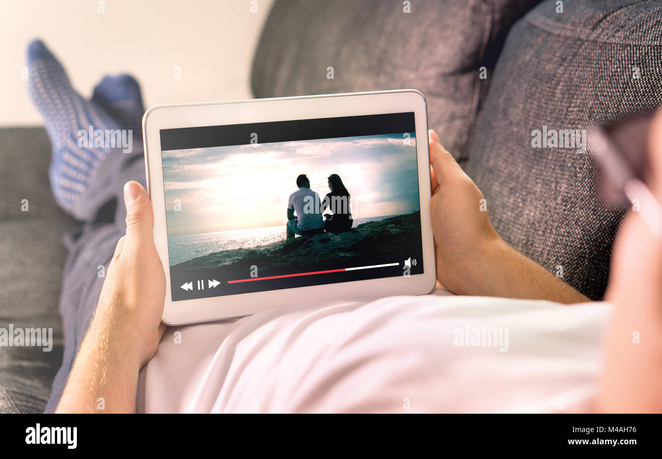 Film en ligne flux avec appareil mobile. Man Watching film sur tablette avec lecteur vidéo imaginaire service. Banque D'Images