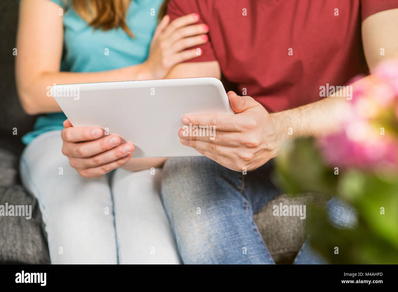 Happy couple using tablet ensemble à table. Young man and woman browsing internet ou regarder la télévision ou un film stream en ligne sur appareil mobile intelligent. Banque D'Images