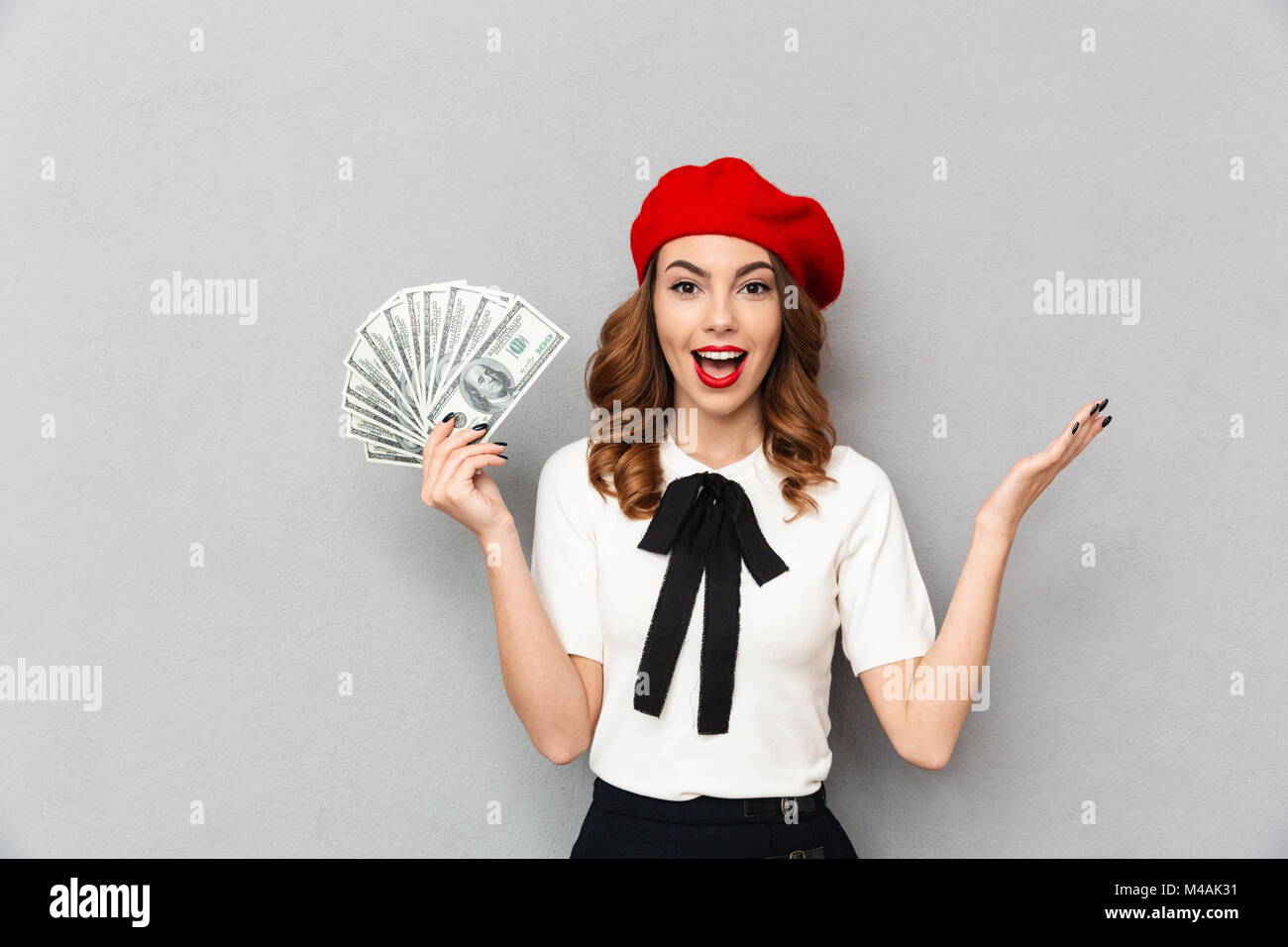 Portrait d'une écolière excité habillés en tenue uniforme tas de billets et de l'argent à la caméra au fond de mur gris plus isolés Banque D'Images