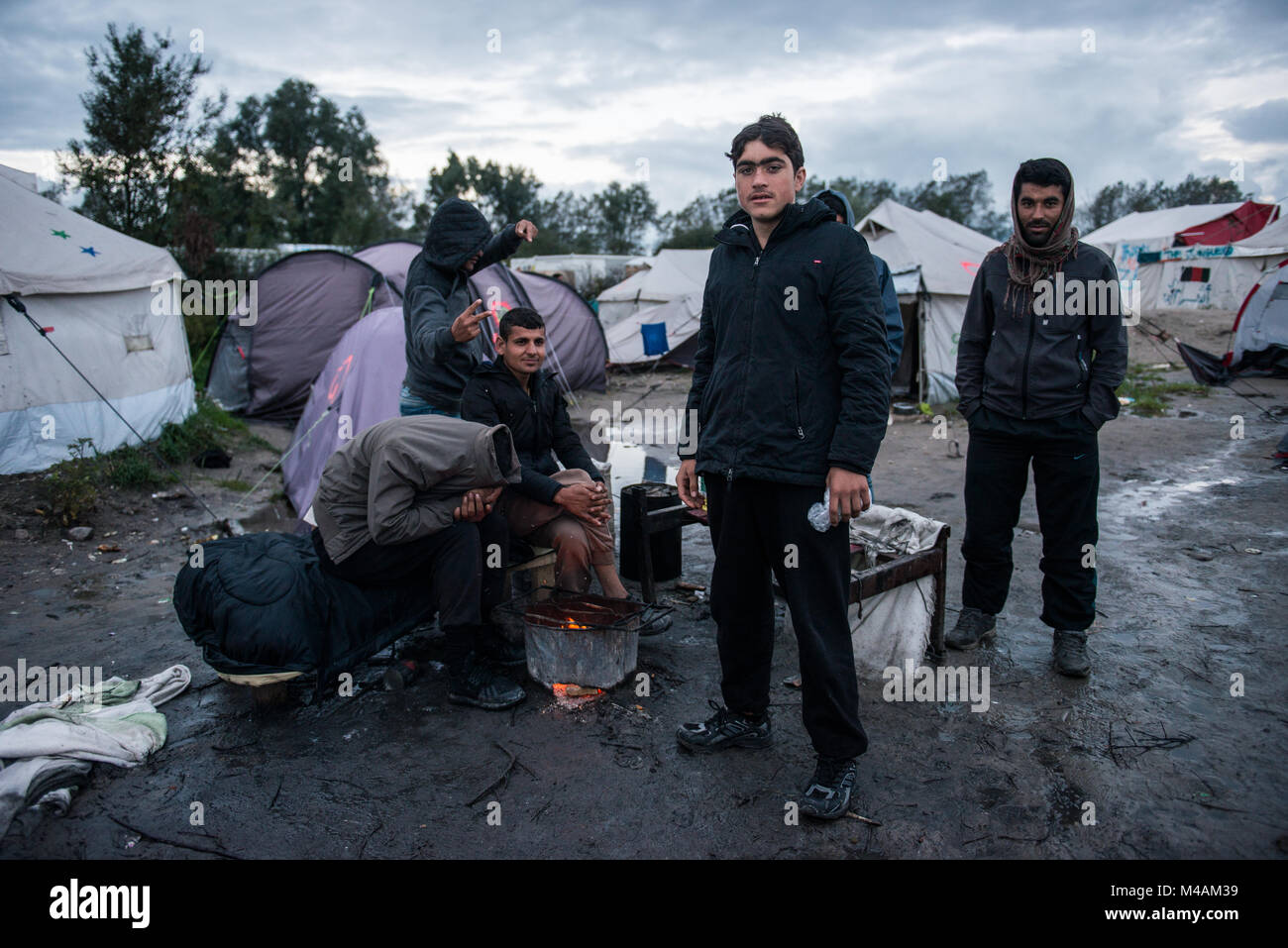 Un groupe d'afgan personnes autour du feu, après quelques heures de pluie intense dans la jungle de Calais. Banque D'Images