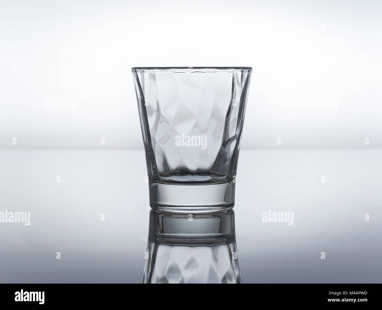 Petit verre isolé dans un fond gris avec reflet Banque D'Images