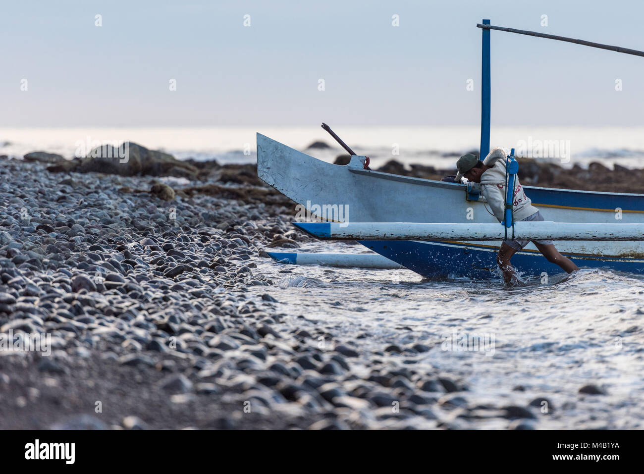 Pêcheur balinais est de retour de la pêche et pousse sa pirogue (Jukung) à la plage de gravier Banque D'Images