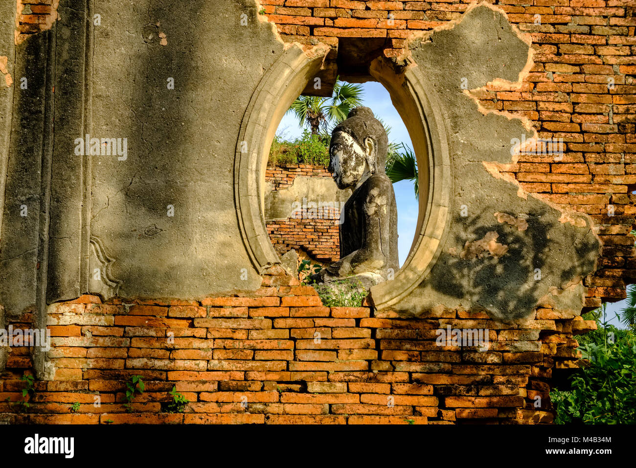 Une statue de bouddha est assis dans le bâtiments en brique de la Pagode Yadana Hsemee dans complexe Inwa, ancienne capitale de la Birmanie, vu à travers une fenêtre dans une brique Banque D'Images