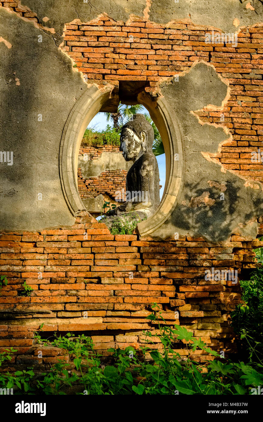 Une statue de bouddha est assis dans le bâtiments en brique de la Pagode Yadana Hsemee dans complexe Inwa, ancienne capitale de la Birmanie, vu à travers une fenêtre dans une brique Banque D'Images