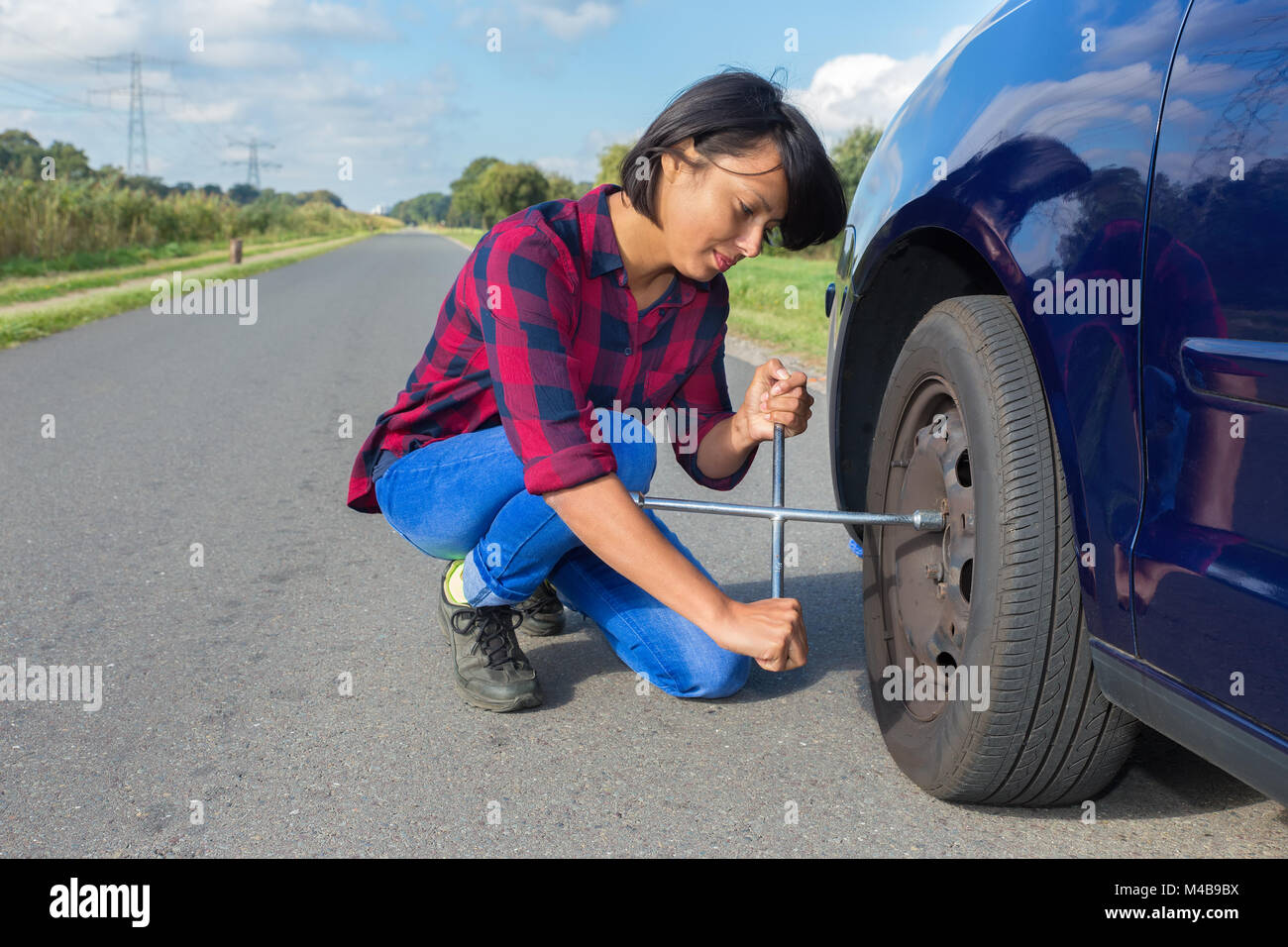 Jeune femme changer de roue de voiture on country road Banque D'Images