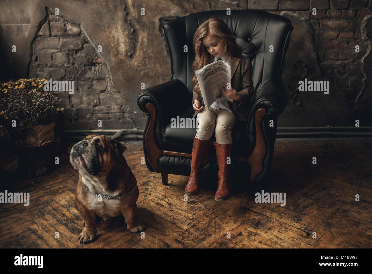 Fille de l'enfant dans l'image de Sherlock Holmes est assis dans un fauteuil et lit un journal à côté de bulldog Anglais sur fond de murs en briques anciennes et minable parque Banque D'Images