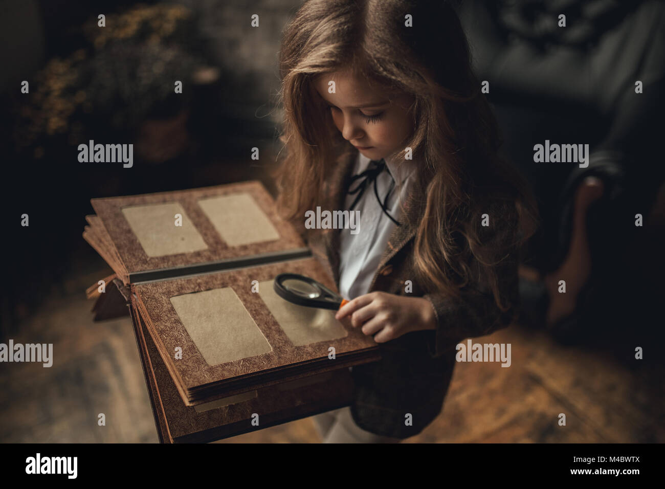 Fille de l'enfant dans l'image de Sherlock Holmes se trouve dans la pièce et l'air vieux photoalbum avec loupe à la main sur fond de fauteuil et vieille défraîchie par Banque D'Images