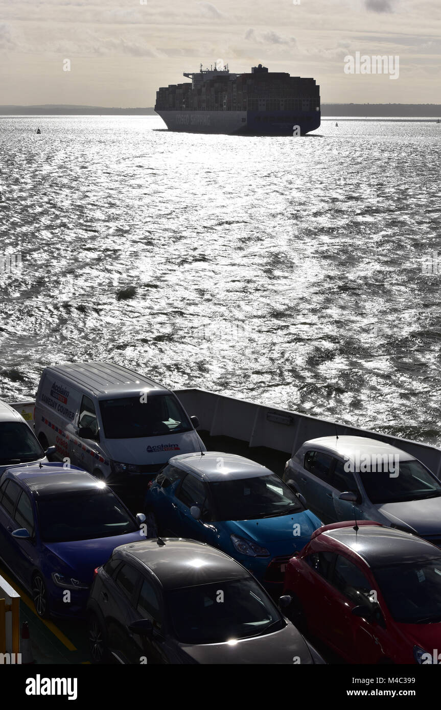 Les voitures sur le pont de l'île de Wight car-ferry d'être transportés à travers le Solent à l'île au coucher du soleil avec un grand récipient shipat au coucher du soleil. Banque D'Images