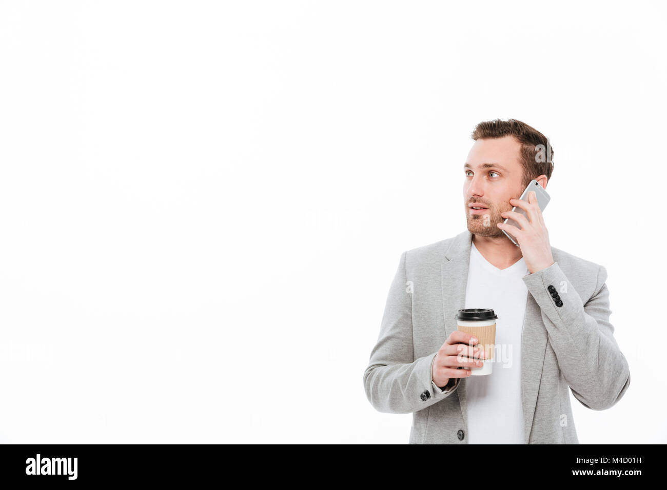 Portrait of male office worker de boire du café à emporter tout en ayant une conversation sur téléphone portable mobile agréable et à côté sur mur blanc Banque D'Images