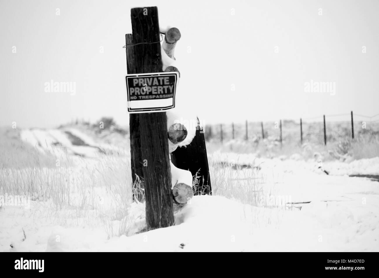 Un ancien pneu appuyé contre un poteau de clôture dans le désert de l'Utah patché avec la neige en noir et blanc. Banque D'Images