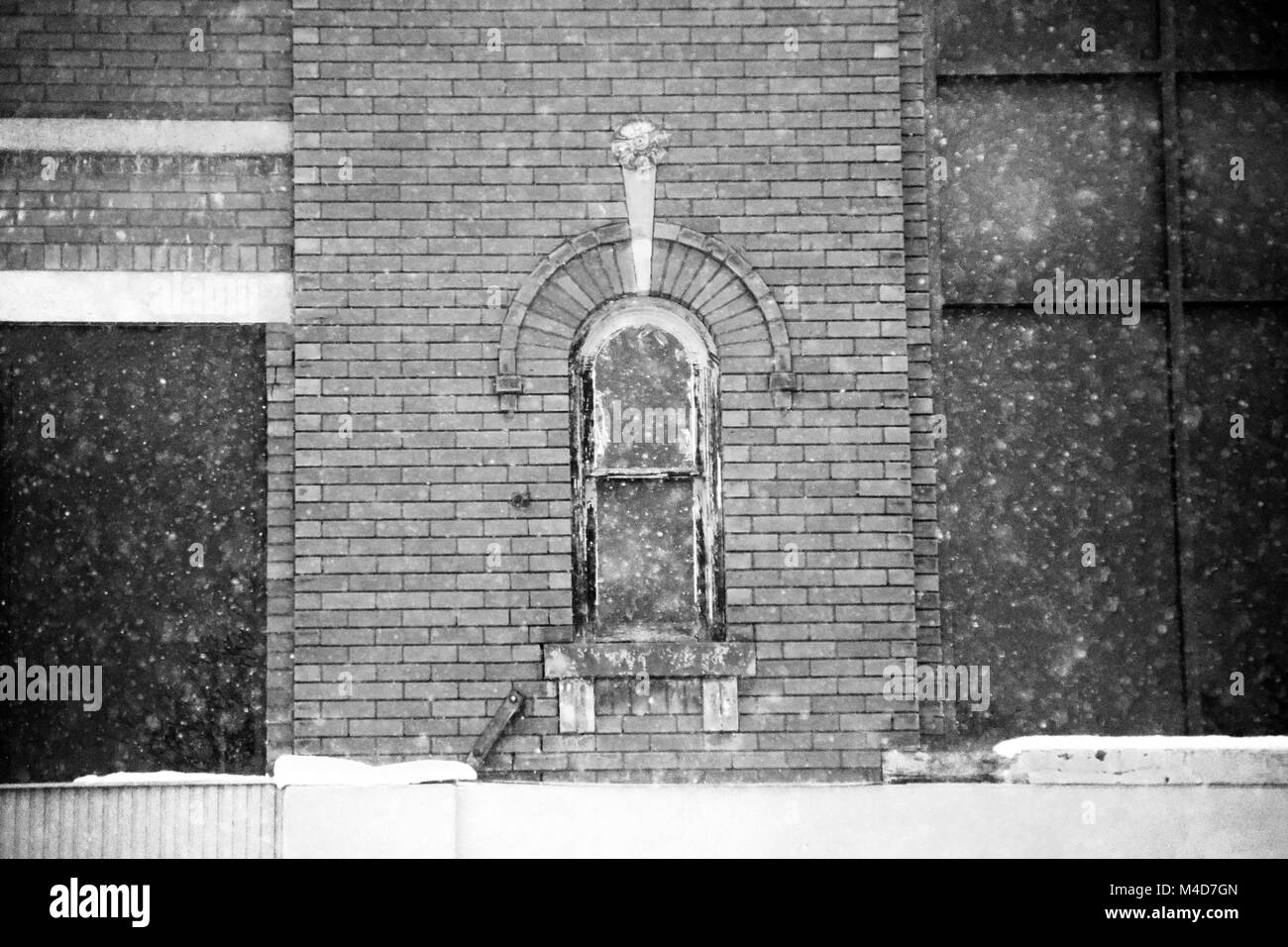 Une vieille fenêtre encadrée en brique dans un vieil immeuble avec la neige qui tombe en noir et blanc. Banque D'Images