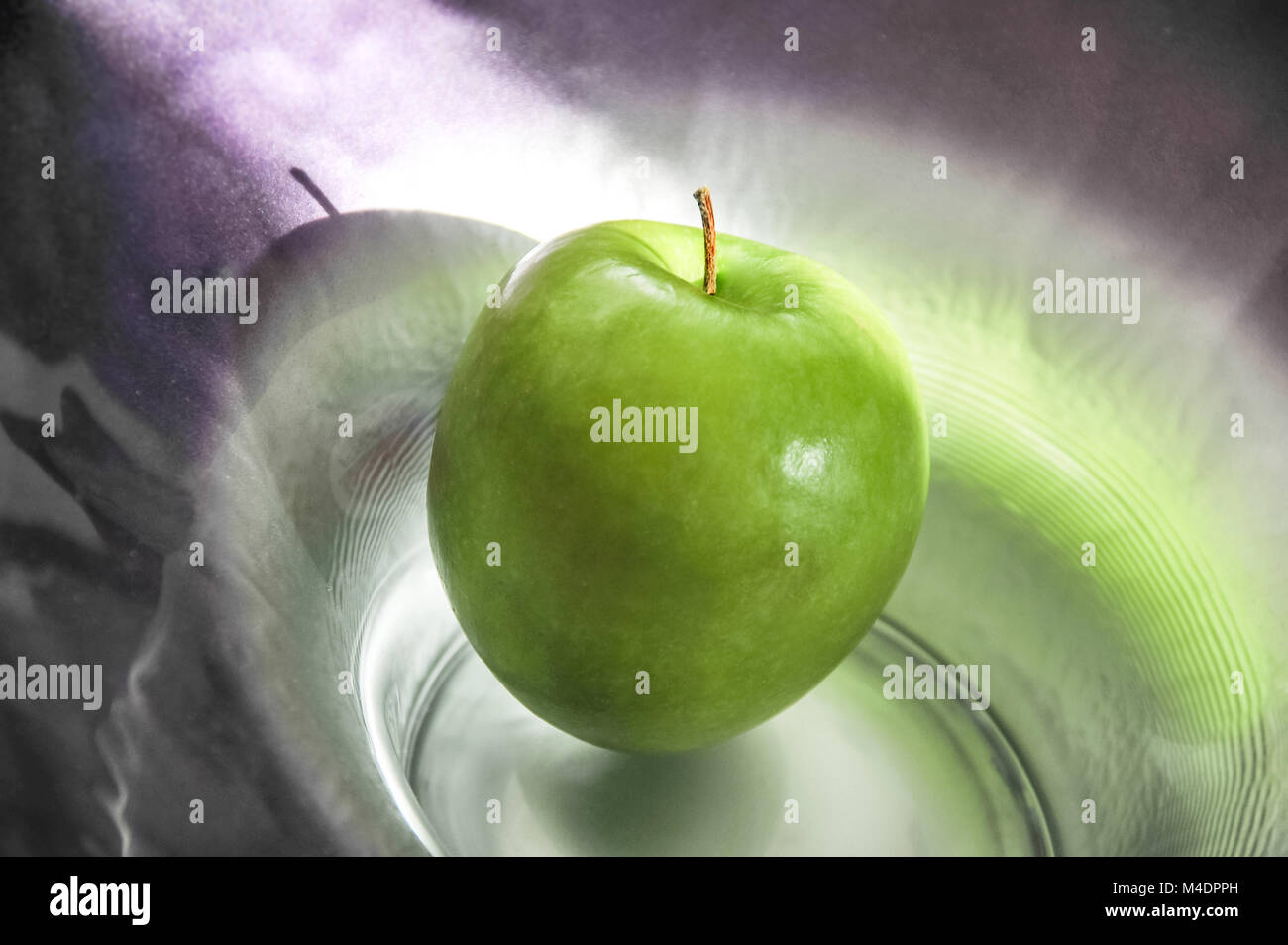 Une pomme verte artistiquement éclairée sur une plaque de verre Banque D'Images