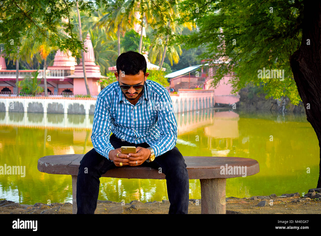 Homme assis sur un banc avec l'arrière-plan du temple à la recherche dans son téléphone cellulaire, Pune, Maharashtra. Banque D'Images