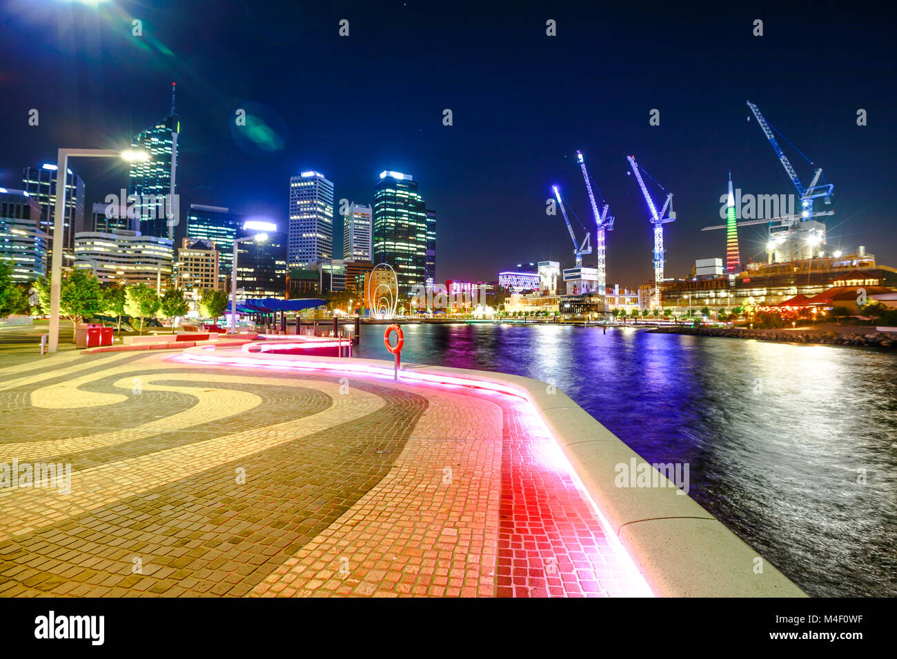 Passerelle à Elizabeth Quay Marina, Esplanade avec les gratte-ciel modernes et les grues de construction sur la rivière Swan à Perth Centre-ville avec l'éclairage de nuit, dans l'ouest de l'Australie. Banque D'Images
