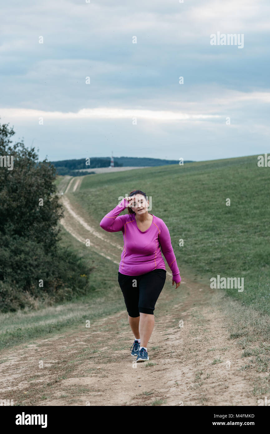 Female jogger voluptueux fatigué d'essayer de reprendre son souffle après un jogging dans un pays. Banque D'Images