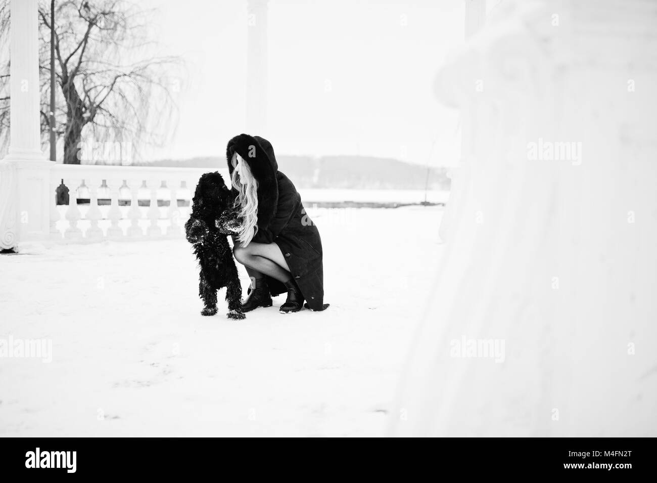 L'élégance blonde en manteau de fourrure câlins petit chien noir à la journée d'hiver. Banque D'Images
