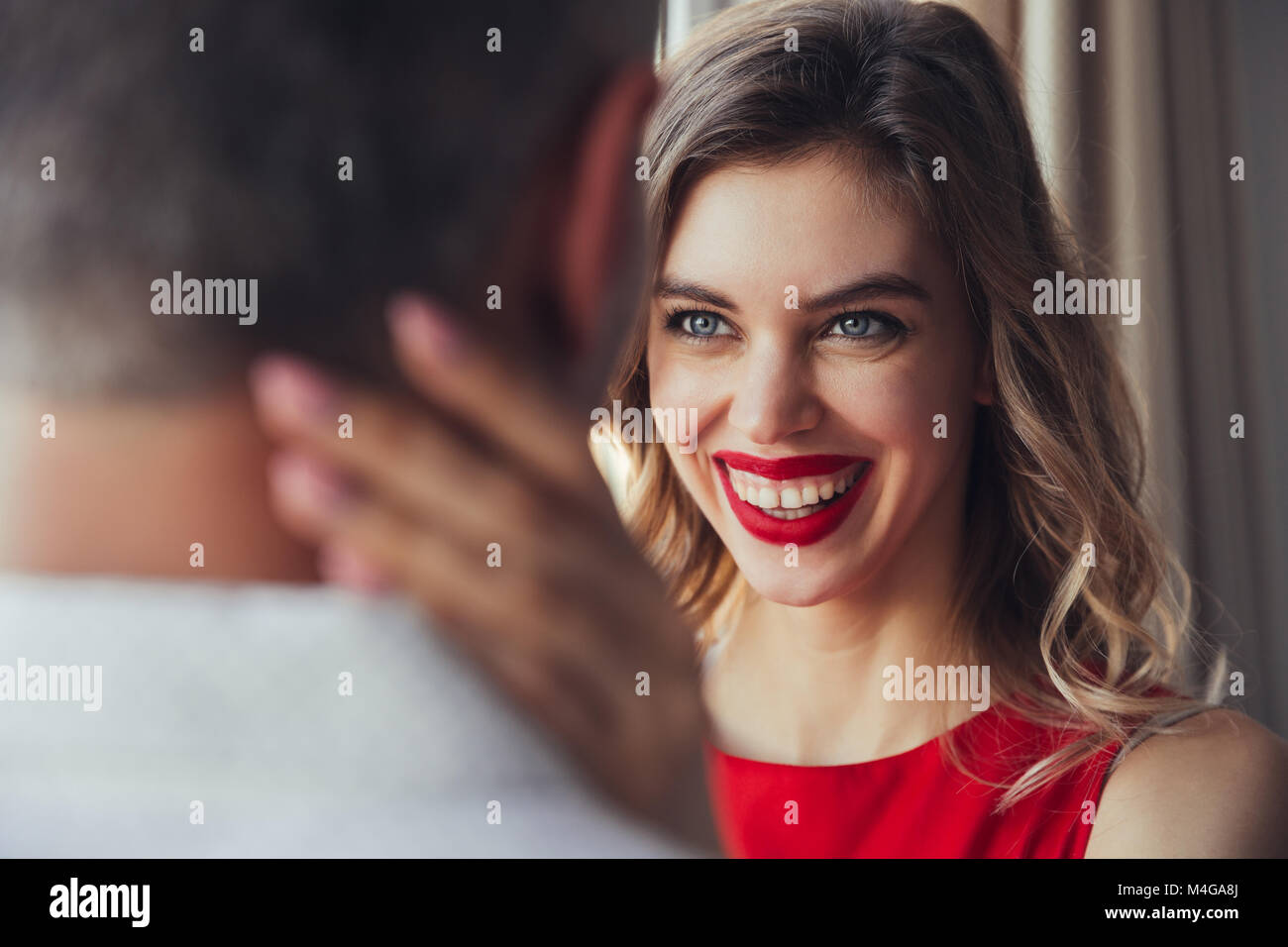 Portrait of laughing woman with red lips embrasser son mari à la maison Banque D'Images
