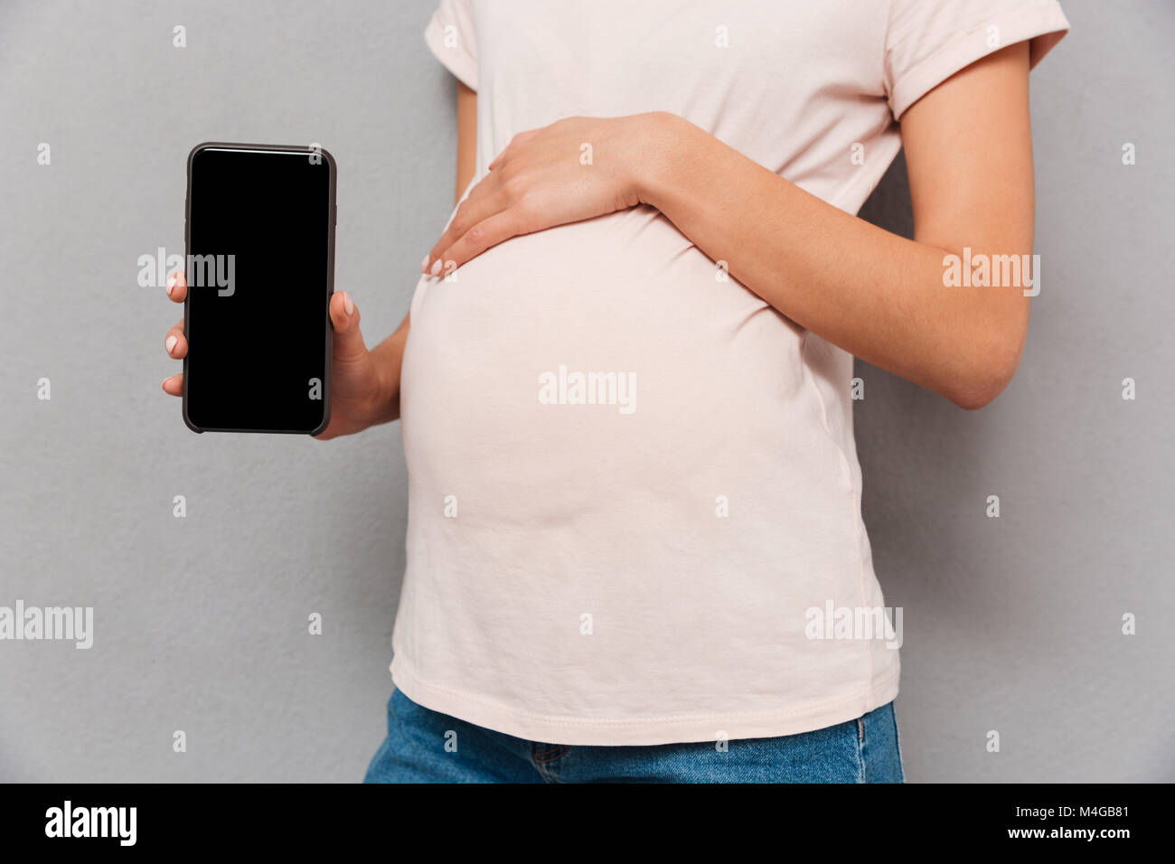 Close up of a pregnant woman's belly avec part montrant écran blanc téléphone sur fond gris Banque D'Images