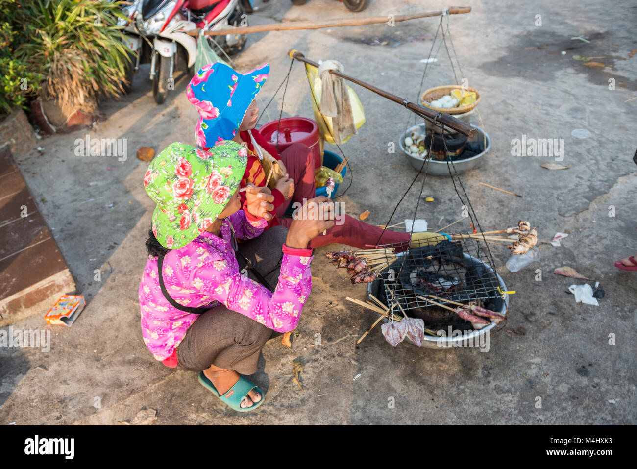 Deux femmes s'accroupir sur le sol préparer et vendre des mollusques grillé sur la plage à Sihanoukville, au Cambodge. Banque D'Images