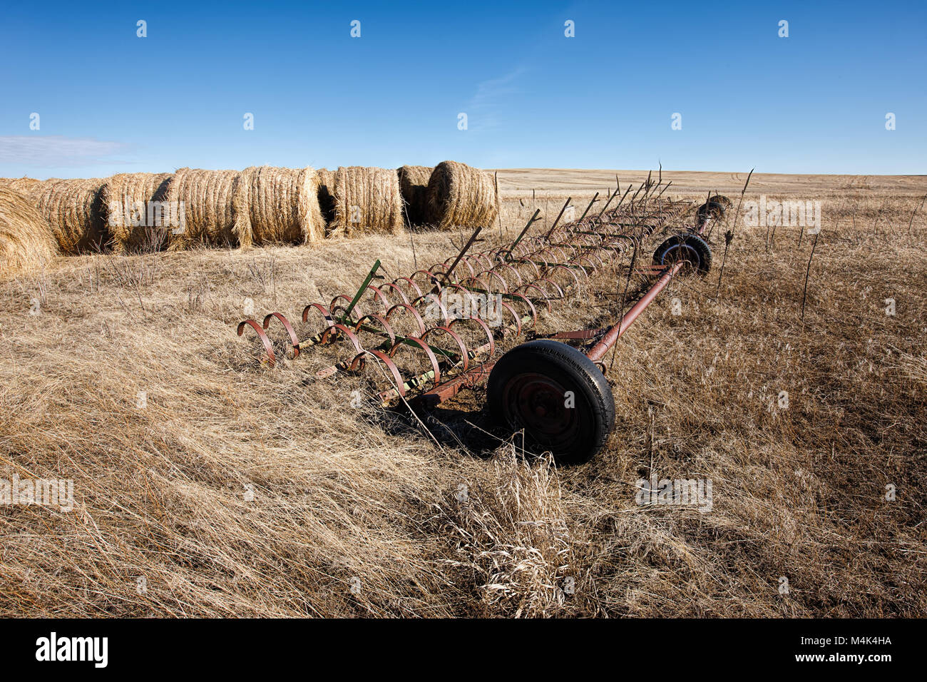 Une pièce d'équipement agricole est assis dans l'herbe par de grandes dales de foin près de Davenport, Washington. Banque D'Images