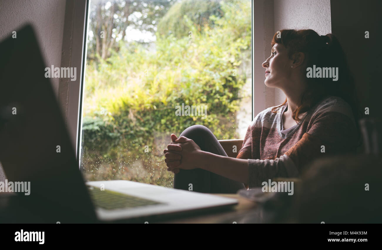 Thoughtful woman sitting near window Banque D'Images