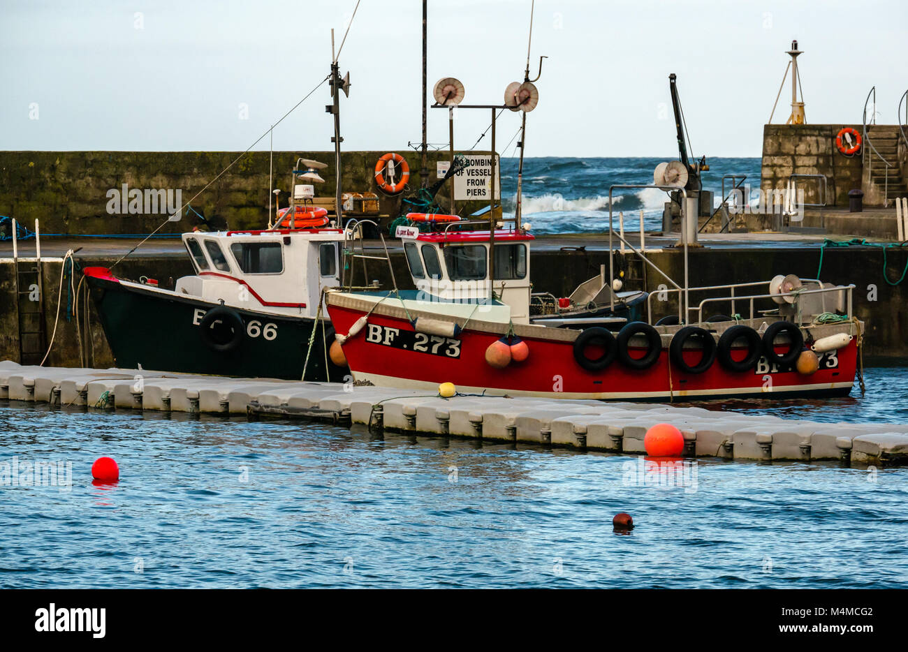 Petits bateaux de pêche dans le port, village de bord de Gardenstown, Aberdeenshire, Scotland, UK, avec les vagues se briser au-delà Mur du port Banque D'Images