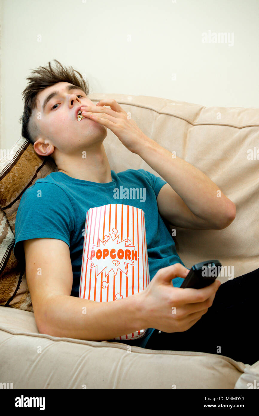 Teenage boy sur un sofa eating popcorn Banque D'Images