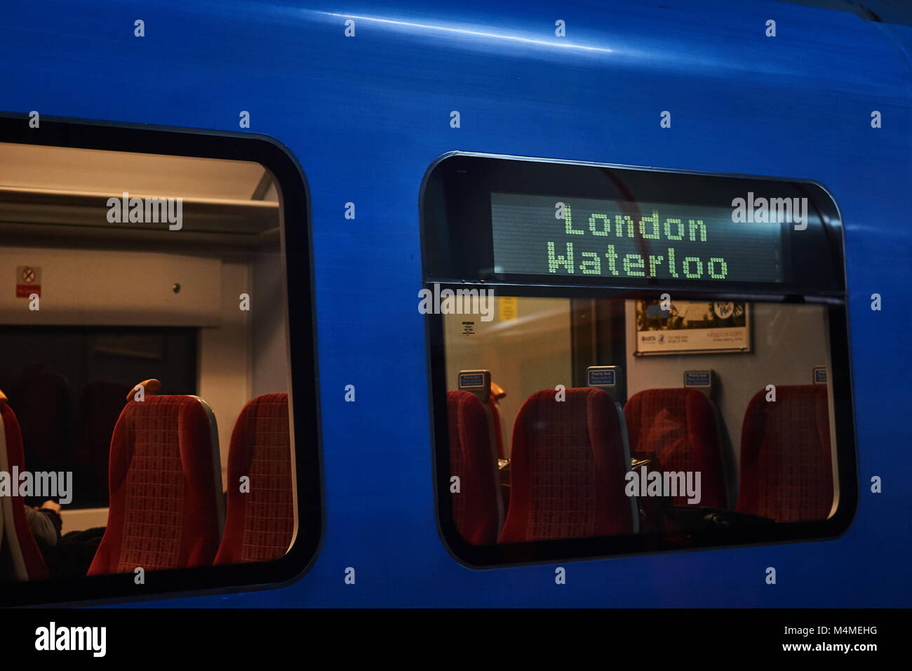 Un Southern Rail train bleu, avec la destination de Londres Waterloo montrant sur le côté du train, les sièges à l'intérieur du chariot visible à la station d'attente Banque D'Images