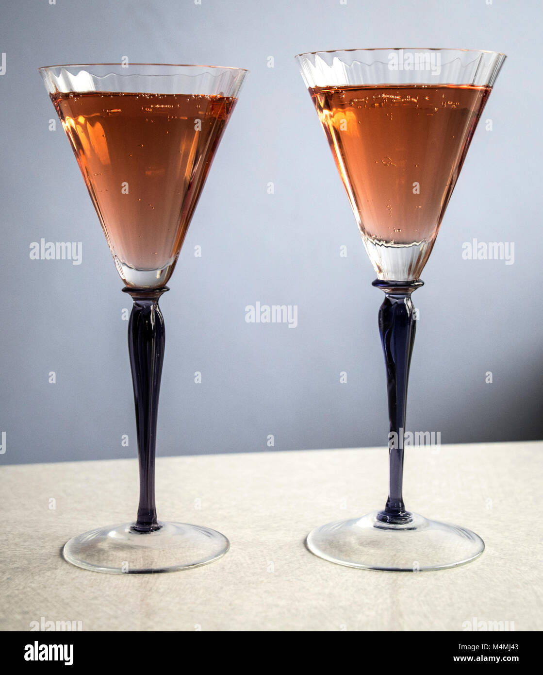 Deux verres, tiges pourpres avec champagne rose sur fond clair Banque D'Images