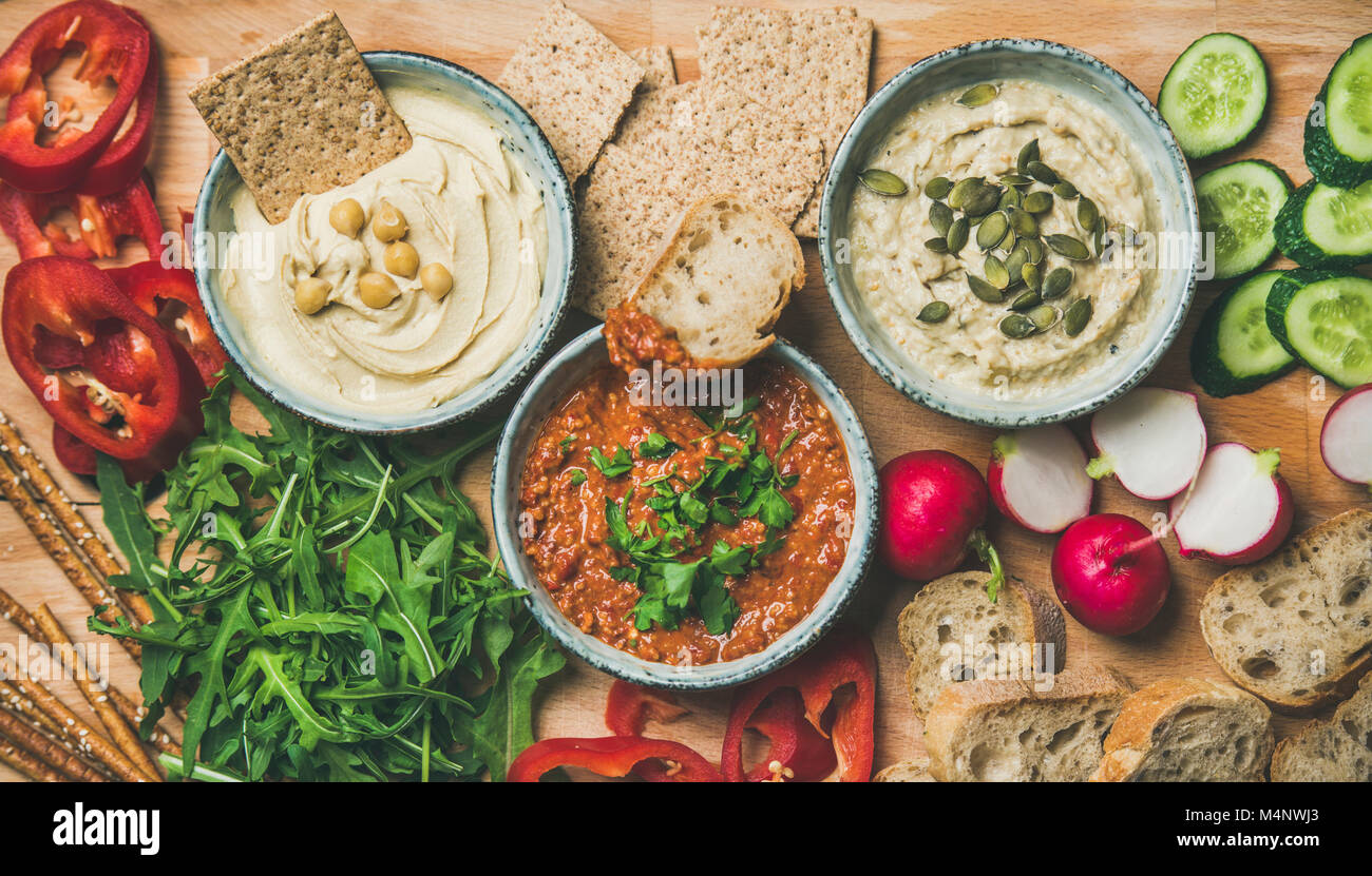 Vegan snack-conseil. Télévision-laïcs de divers dips végétarien, de l'hummus et babaganush muhammara avec des craquelins, du pain et des légumes frais, fond de bois, Banque D'Images