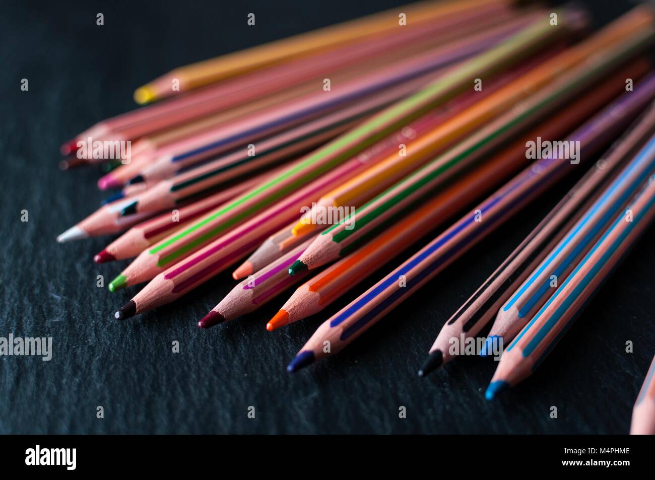 Une gamme de crayons de couleur sur une ardoise noire Banque D'Images