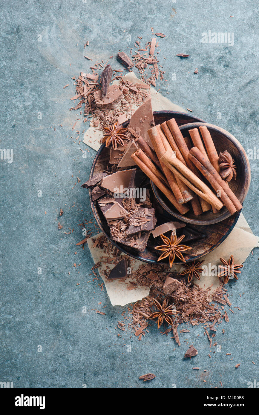 Châssis avec un bol en bois rempli de pièces en chocolat, d'épices, d'anis étoile, la cannelle et cacao sur un fond de pierre. Ingrédients pour un dessert. Banque D'Images