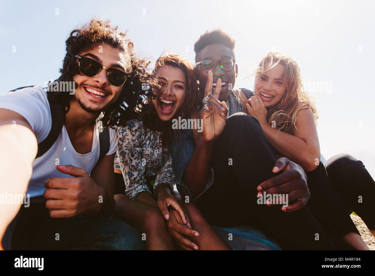 Jeunes amis excité en tenant l'extérieur selfies. Groupe diversifié d'hommes et de femmes siégeant ensemble et taking self portrait sur leurs vacances. Banque D'Images