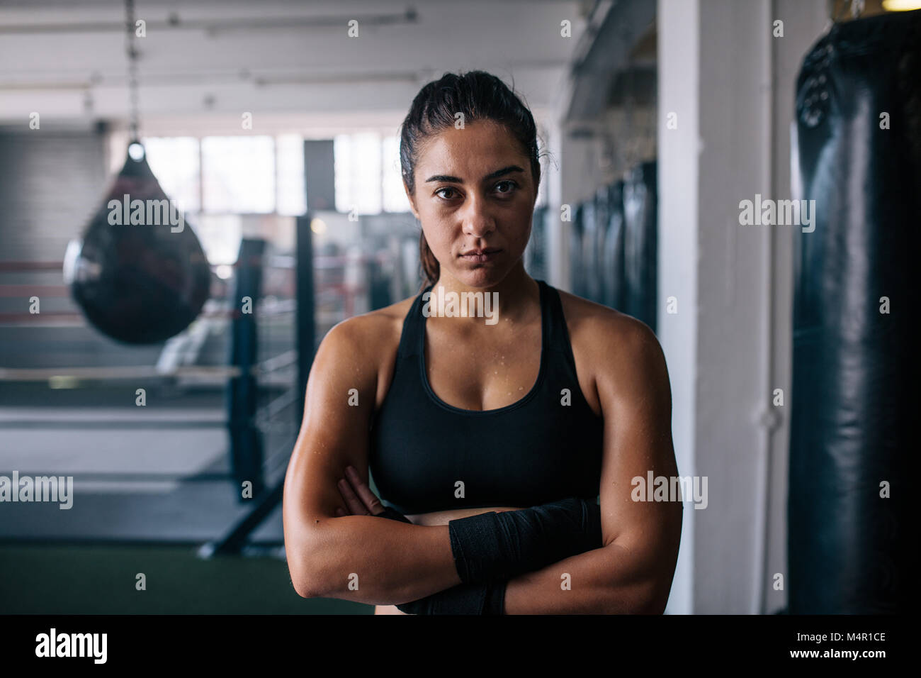 Close up of a female boxer debout à l'intérieur d'un studio de boxe avec ses mains pliées. Femme debout dans un centre d'entraînement de boxe avec sacs de frappe et de bo Banque D'Images