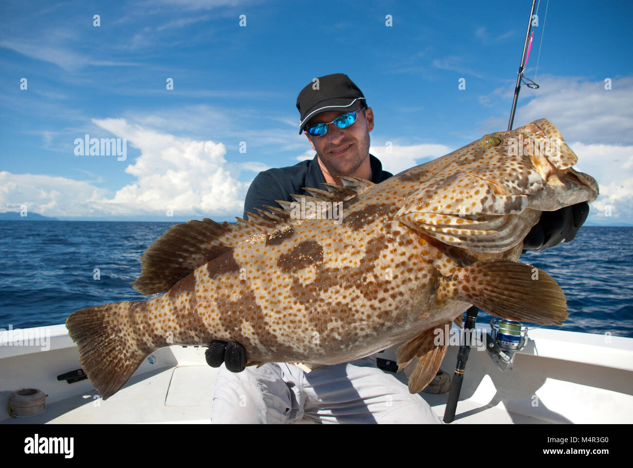 Heureux fisherman holding une belle mérous. La pêche en haute mer, pêche au gros, des prises de poissons. Banque D'Images