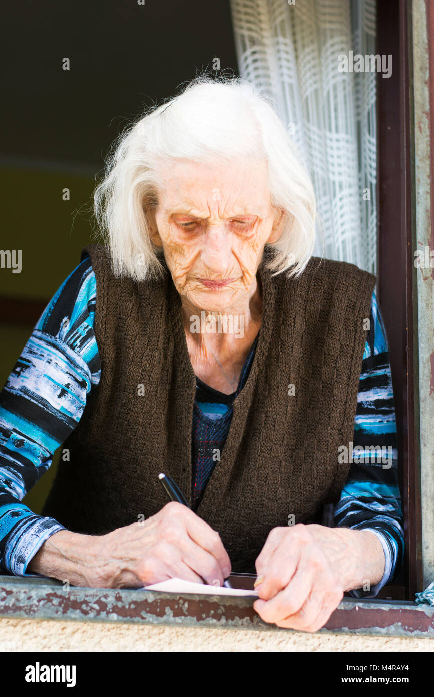 Femme Senior retraite signature vérifier sur la fenêtre à la maison Banque D'Images