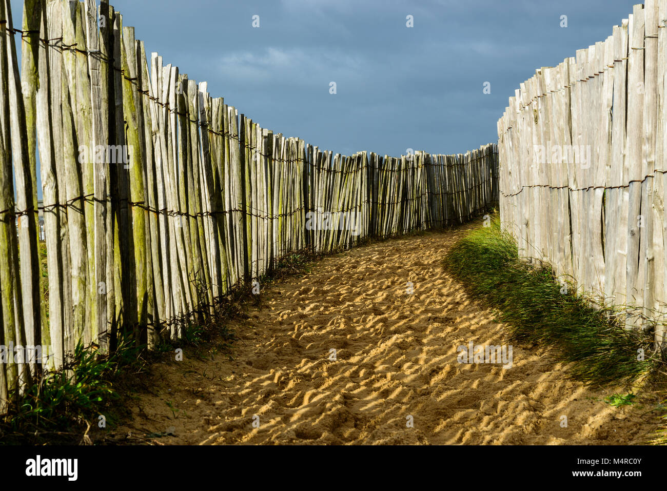 Chemin de sable côtières, barrières en bois foncé dans les deux, et ciel nuageux, en Bretagne, France Banque D'Images