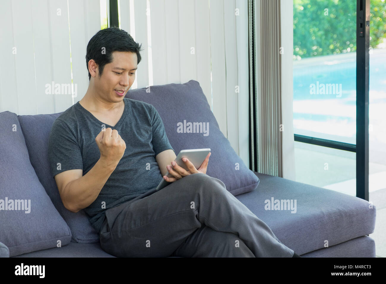 Homme assis sur un canapé et regarder un match de football en direct en streaming sur tablette et jusqu'à bras pour boire de l'équipe.sport digital lifestyle Banque D'Images