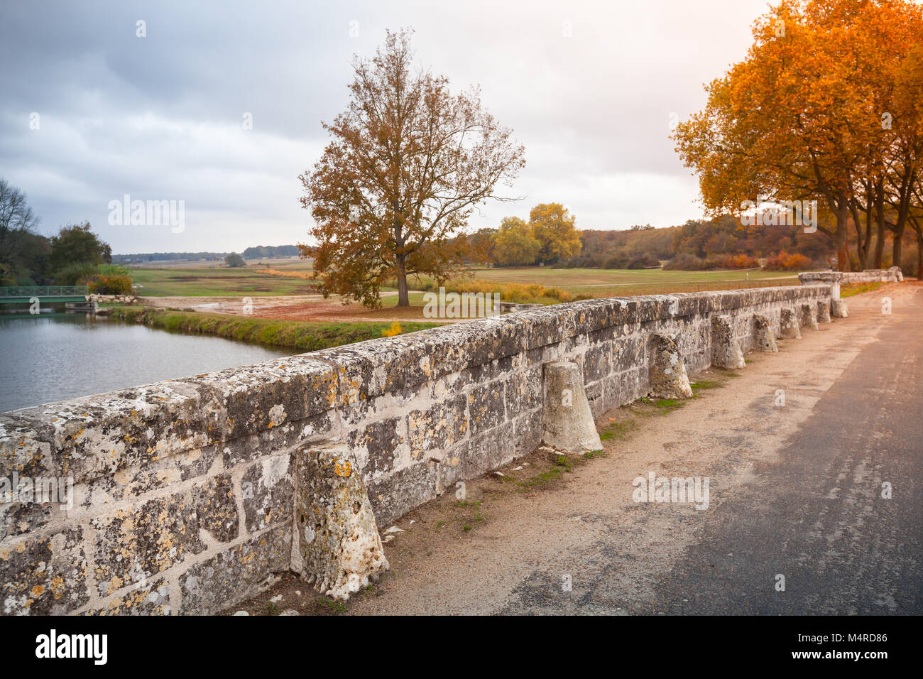 Le paysage du parc français, vieux pont de pierre sur la route et les arbres d'automne Banque D'Images