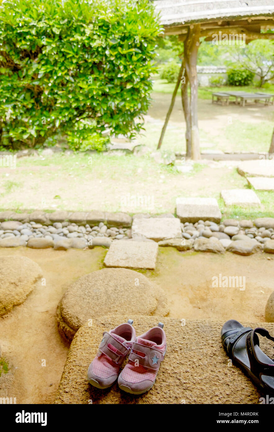 Les chaussures pour enfants rose sur l'étape de la pierre. Sur la droite, 1 noir sandale. Gauche en arrière-plan sont des arbres. Sur la droite une structure rustique. Portrait. Banque D'Images